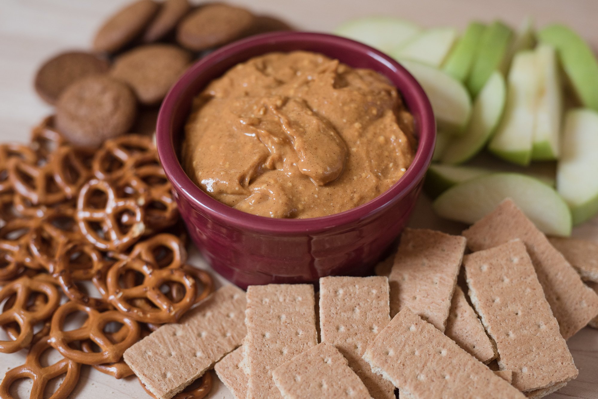 pumpkin dip on cutting board with ginger snaps, pretzels, apples and crackers